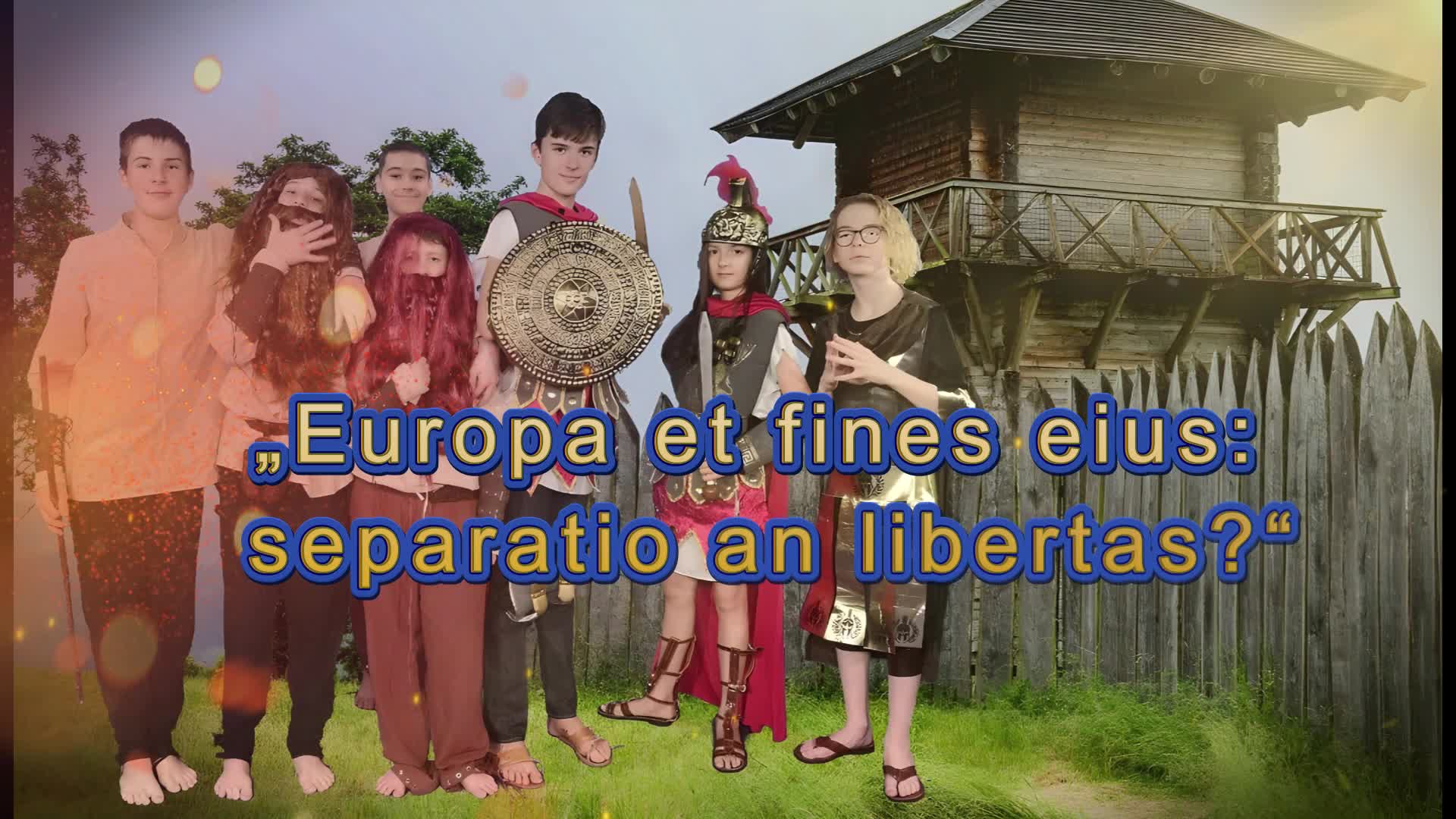 Eine Gruppe von Kindern in historischen Kostümen steht vor einer Holzfestung. Der lateinische Text lautet: 